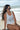 Happy Vibe Quick Dry Racerback Tank Top, White. Model sitting with beach in background